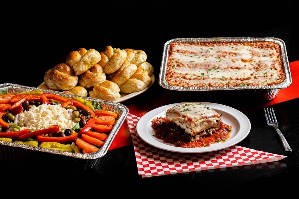 Bambinelli’s catering trays with lasagna, salad, vegetables, and garlic rolls